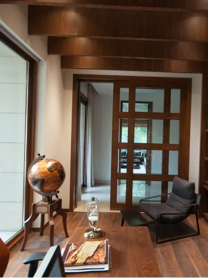 This home office within the 'House of Bridges' is a quiet sanctuary. Rich wood paneling, built-in bookshelves, and a view of the outdoors create a space that is both functional for work and deeply connected to the home's warm aesthetic.