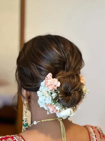 This intricate wedding bun is decorated with a mix of peach and white flowers, creating a soft and elegant look. It’s a perfect hairstyle for a bride wearing a traditional red lehenga.