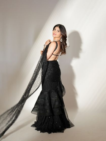 The epitome of cocktail night glamour. This look, featuring a stunning black ruffled saree, is complemented by soft, glowing makeup and a radiant smile.