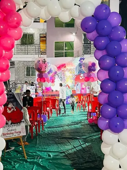 A vibrant balloon arch entrance for an outdoor birthday party. The pink, purple, and white colors welcome guests into the celebration area.
