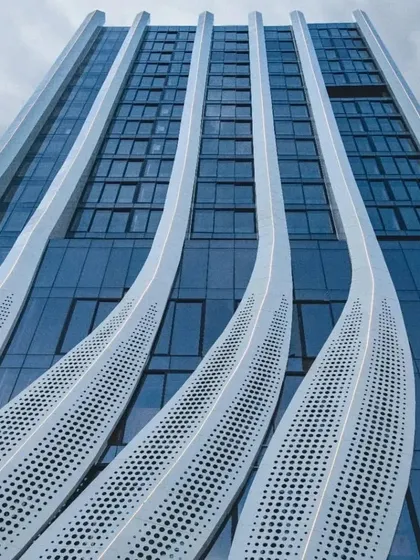 The facade's undulating lines viewed from below, creating a dramatic perspective against the sky. The design balances aesthetic form with functional performance.