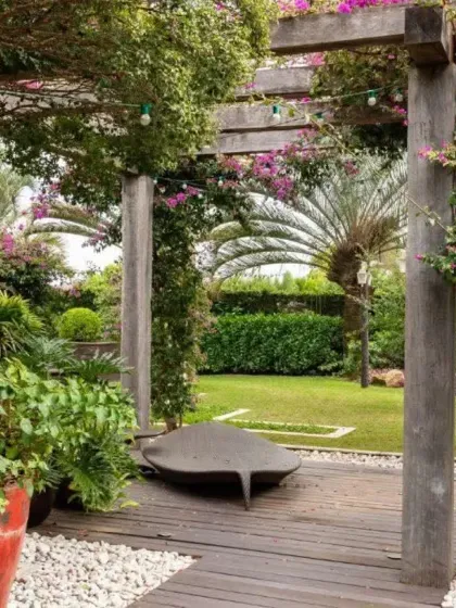 A rustic wooden pergola creates an intimate seating area, enveloped by flowering bougainvillea climbers. This is a perfect example of how I use hardscaping and softscaping to build beautiful and functional outdoor living rooms.