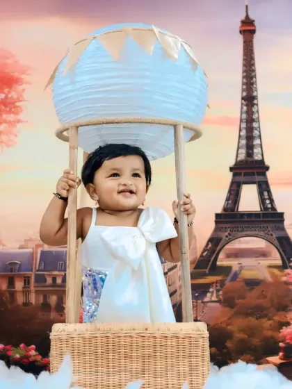A dreamy Parisian adventure, with a smiling baby in a hot air balloon prop set against a romantic Eiffel Tower backdrop at sunset.