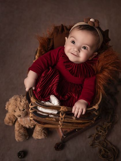 The younger sibling takes her turn in the spotlight. This sweet baby girl, dressed in a beautiful red velvet dress, looks so content in her cozy basket.