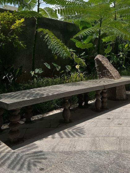 A custom-designed stone bench with ornate carved legs and a raw, natural stone backrest. This piece combines traditional craftsmanship with raw natural materials, creating a unique and functional sculpture.