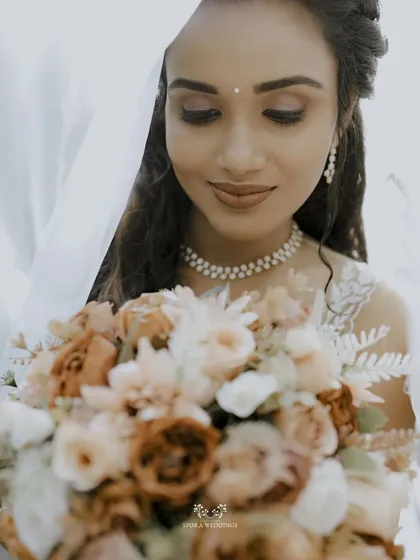 A delicate close-up of the bride looking down at her bouquet, her pearl necklace and soft makeup adding to her timeless beauty.