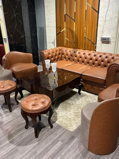 A classic living room setup featuring a brown leather Chesterfield sofa, matching tufted stools with cabriole legs, and complementary armchairs. This collection exudes a warm, traditional, and clubby feel.
