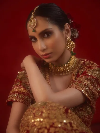 A traditional bridal look with a red and gold lehenga, complemented by classic gold jewelry and a soft, romantic makeup look.