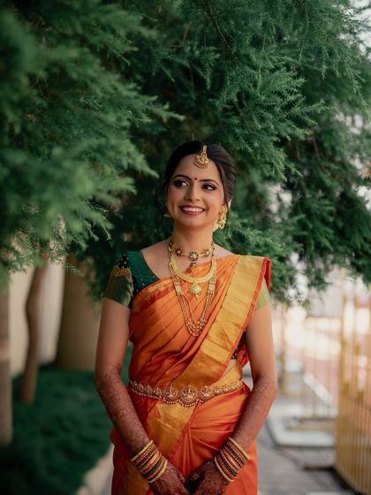 A smiling portrait against a natural green background, her makeup looking fresh and radiant.