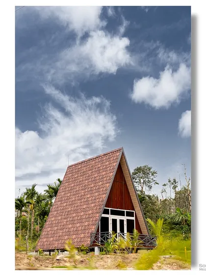 A classic A-frame cabin stands proudly against a bright blue sky in the coffee plantations of Sakleshpur. This image highlights the simple, iconic geometry of the structure and its beautiful rural setting.