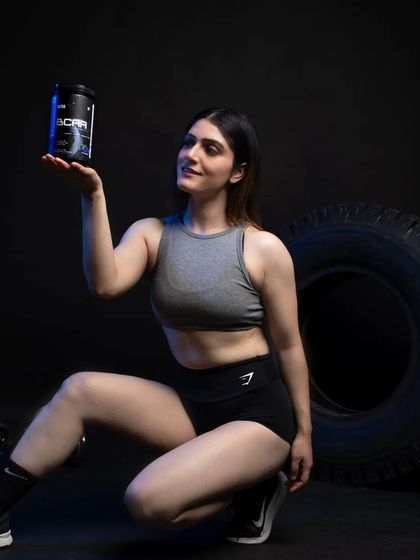 A creative pose where the model presents the BCAA product as a valuable item. The low angle and focused lighting make the product feel premium and essential to her fitness routine.