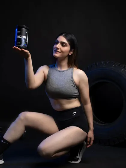 A creative pose where the model presents the BCAA product as a valuable item. The low angle and focused lighting make the product feel premium and essential to her fitness routine.