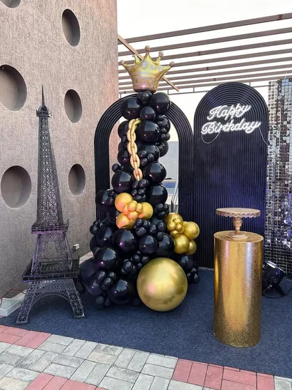 For a sophisticated adult birthday on a terrace, I designed this chic black and gold theme. The setup includes a statement balloon sculpture with a crown, a miniature Eiffel Tower for a touch of Parisian elegance, and a glowing neon sign, creating a perfect photo-op spot.