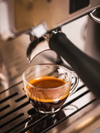 A finished shot of espresso in a glass cup, sitting on the machine's drip tray. This clean, final-product shot is perfect for menus or websites.