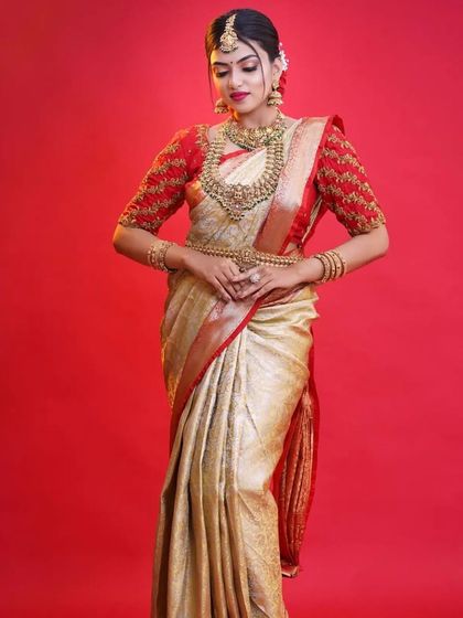 A full view of a bride in a classic cream and red saree, perfectly complemented by our temple jewellery. The Vaddanam completes the traditional look.