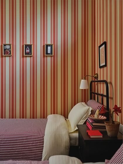 The guest bedroom, wrapped in terracotta and cream striped wallpaper, offers a cocoon-like embrace. A pair of vintage-style twin beds and framed artworks create a familiar sense of comfort.