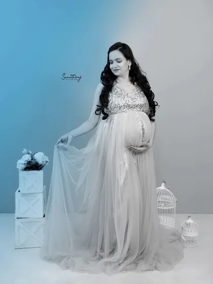 A dreamy, artistic portrait in a flowing silver gown. The blue color grading and ethereal props like the birdcage add a magical and unique touch to this indoor shot.