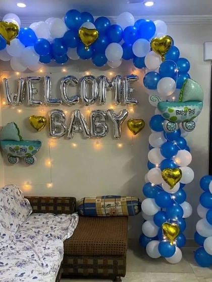 A classic "Welcome Baby" setup for a baby boy. This decoration features a blue and white balloon arch, silver foil letters, fairy lights, and cute baby-themed foil balloons.