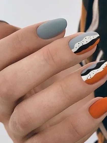 This design showcases the beauty of matte finish nail art. It combines solid orange and grey nails with an abstract pattern in black, white, and orange for a sophisticated, textured look.
