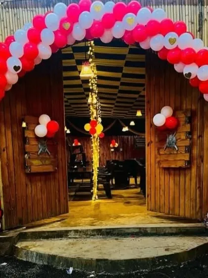 A classic red and white balloon arch creating a grand entrance for a party at a venue with a rustic, wooden facade.