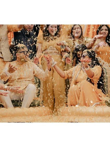 The couple reacts with joy as they are covered in a blizzard of flower petals during their haldi.