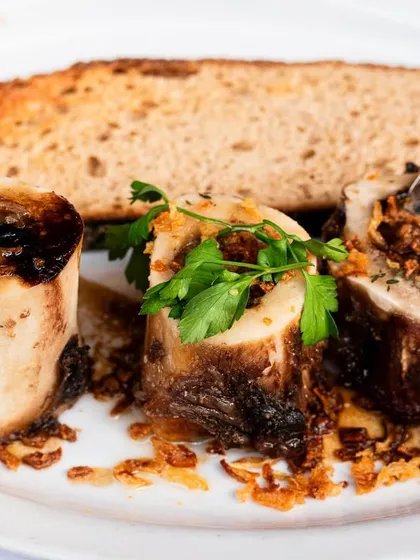 An elegant dish of roasted bone marrow with toast. The plating and lighting convey a sense of a classic, upscale French bistro experience.