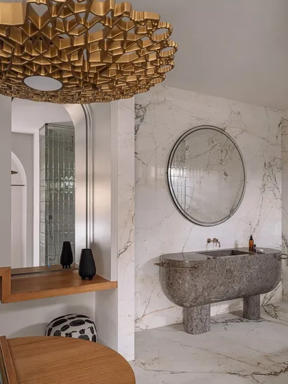 This walk-in wardrobe and bathroom was designed to feel like a high-end SoHo boutique. It features a sculptural, monolithic marble basin, an island dresser, and custom clothing racks, all set against a backdrop of luxurious veined marble.
