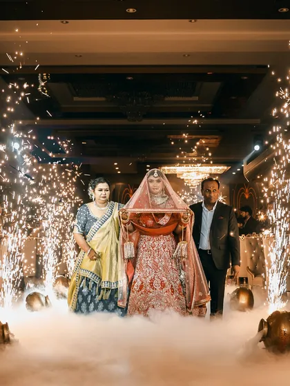 The bride's grand entrance, walking under a phoolon ki chadar held by her parents. This shot, filled with smoke and sparklers, captures the drama and emotion of this key wedding moment.