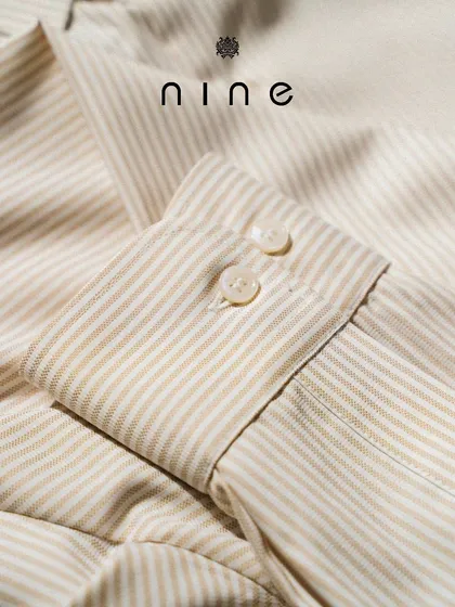 A close-up of the cuff on our beige and white striped summer shirt. The precise stitching and quality buttons are hallmarks of our craftsmanship.