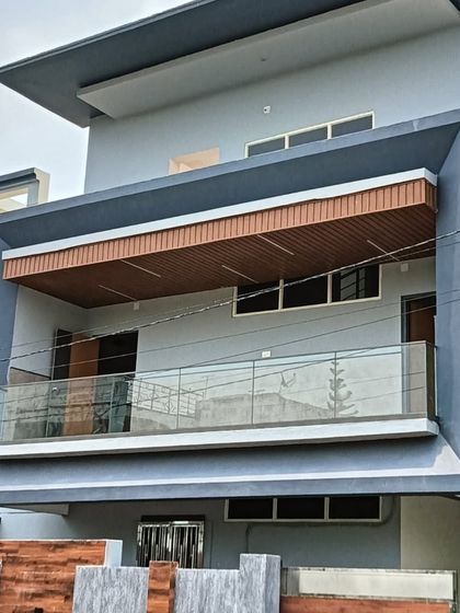 A modern house facade featuring our work. We installed the sleek glass railings and the wood-finish ceiling for the large balcony, creating a clean and contemporary elevation.