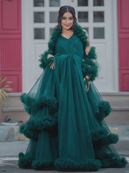 A full-length view of the dramatic, multi-layered green gown. The makeup is kept classic to balance the statement dress.