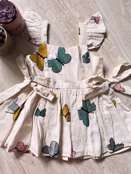 A flat lay of our beautiful butterfly dress. You can see the lovely embroidery and the side ties that make for a perfect fit. It's crafted with so much love.