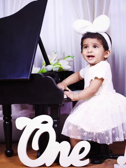 A little girl in a white dress and mouse ears, happily playing our miniature piano.