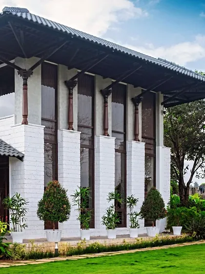 The facade of the classical farmhouse, with its tall columns and potted topiary, stands proudly amidst the green landscape.