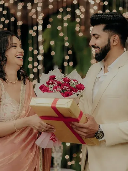The couple exchanging gifts and flowers in front of a backdrop of beautiful fairy lights, a heartwarming part of their engagement story.