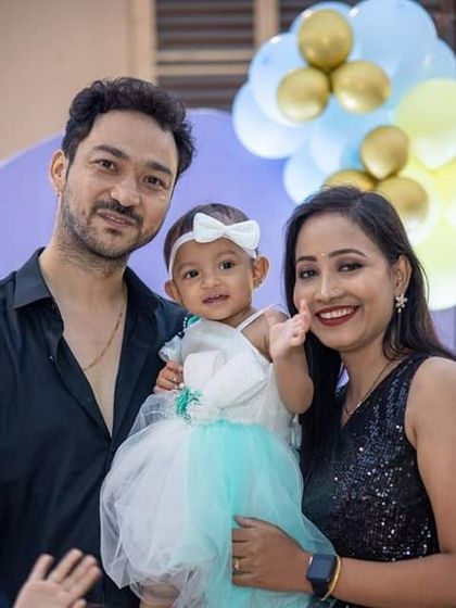 A cheerful family picture with the birthday girl waving to the camera, surrounded by festive balloons.