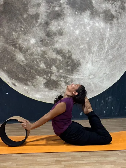 Using props like the yoga wheel allows for deeper exploration of poses. Here, a student gracefully opens her heart and spine in a supported backbend, finding new levels of flexibility against the serene backdrop of our studio.