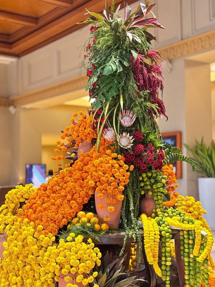 This view highlights the height and texture of the floral masterpiece. The mix of marigold garlands, loose blooms, and tall green foliage creates a dynamic and visually captivating arrangement.