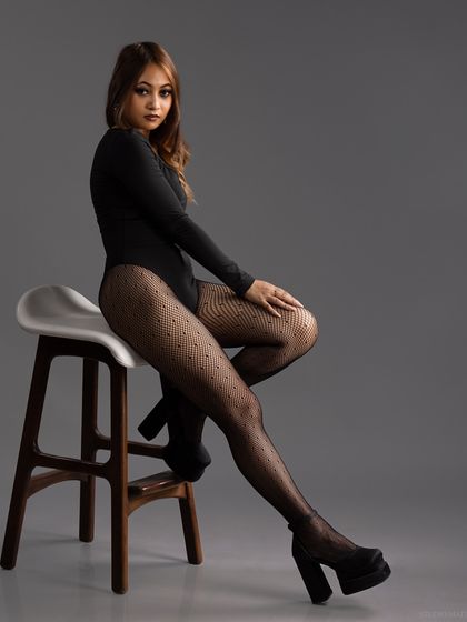 A seated pose in a bodysuit and patterned stockings, with a classic and elegant feel.
