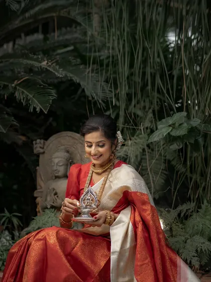The gentle light and lush background highlight the beauty of the bride and her traditional red saree, a classic choice for any South Indian wedding.