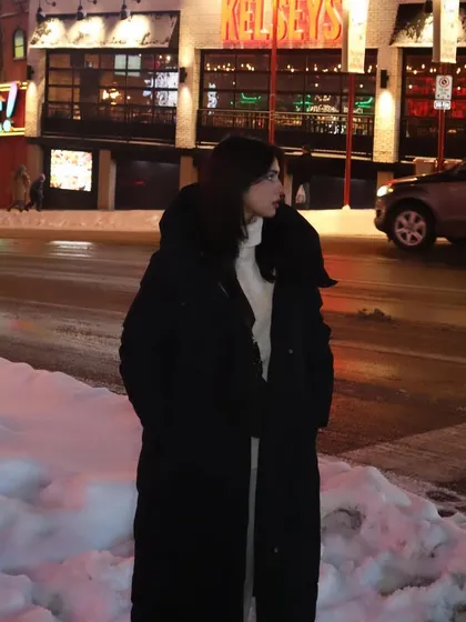 A full-length profile shot showing the long winter coat against the snowy street.