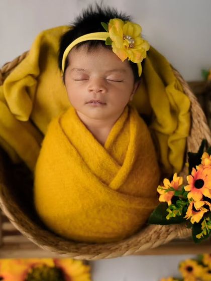 A newborn wrapped in a vibrant yellow blanket rests in a wicker basket, surrounded by sunflowers for a cheerful and sunny portrait.