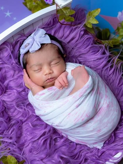 A sweet newborn girl swaddled and sleeping in a white miniature bed, surrounded by purple fur and flowers. This is part of my popular purple theme series.