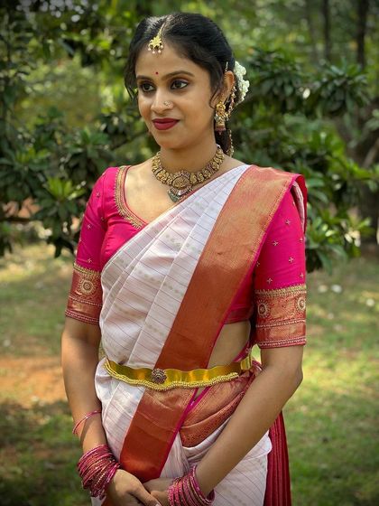 A classic South Indian bridal look with a white Kanchivaram featuring a red and gold border, paired with a vibrant pink blouse with delicate embroidery.