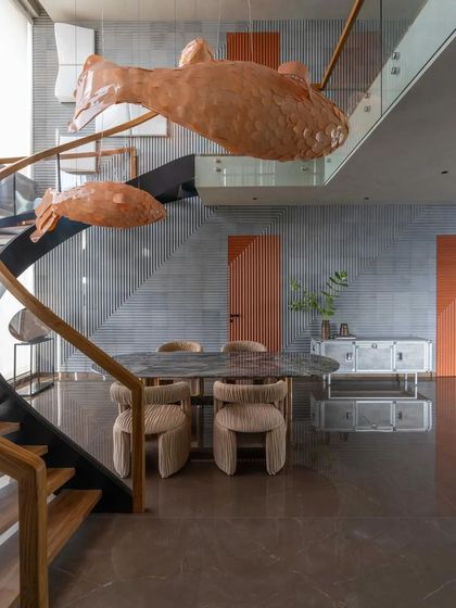The dining area of this Vizag home is dominated by a dramatic, custom light installation of giant, sculptural fish that appear to swim through the double-height space.