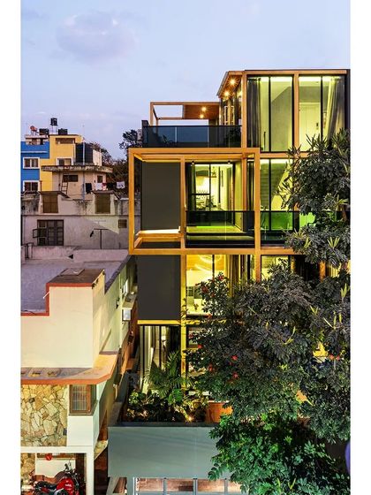 The SOL House at dusk, with its interior lights illuminating the golden structural frame. The design transforms the building into a lantern-like object in the evening, highlighting the relationship between the solid and void spaces.