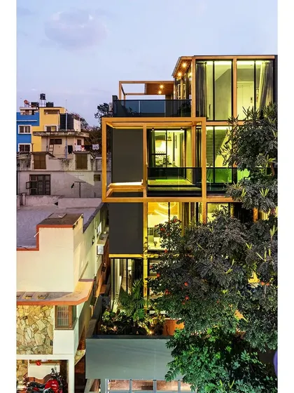 The SOL House at dusk, with its interior lights illuminating the golden structural frame. The design transforms the building into a lantern-like object in the evening, highlighting the relationship between the solid and void spaces.