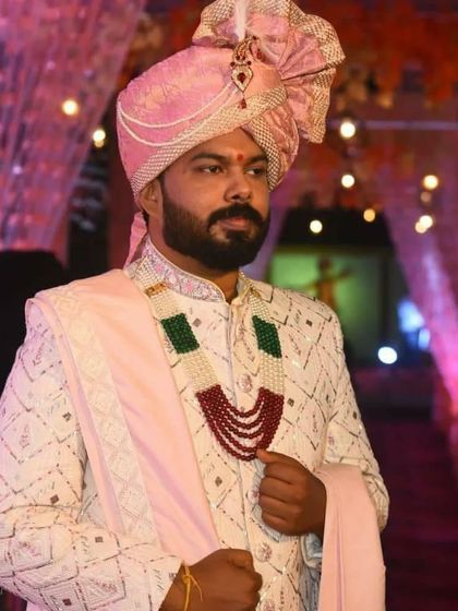 A close-up portrait of a groom, providing a clear view of the texture and embroidery on his off-white sherwani, paired with traditional wedding jewelry.