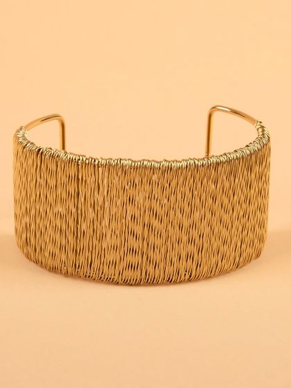 A wide, gold-tone cuff bracelet with a woven wire texture, presented simply to highlight its intricate craftsmanship.