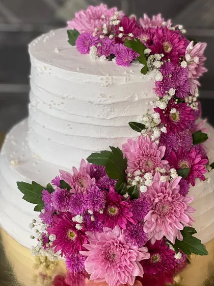 A two-tiered white cake decorated with a cascading arrangement of fresh purple and pink flowers. This design is perfect for weddings, offering a touch of natural beauty and elegance.